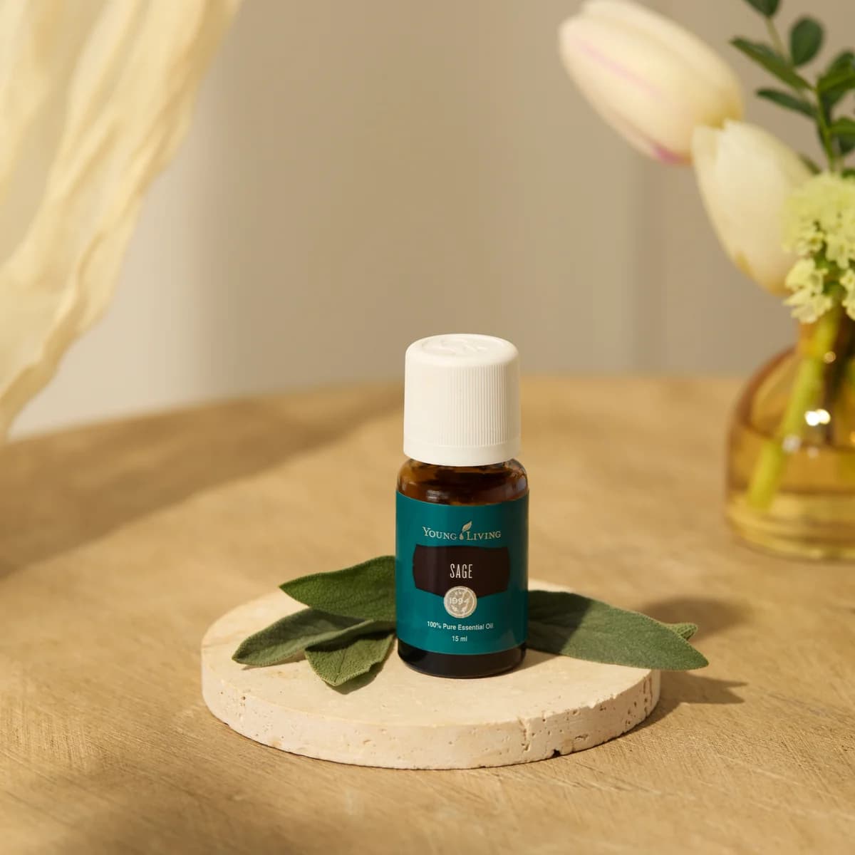 Ein Fläschchen Young Living Salbeiöl 15 ml steht auf einem runden Steinuntersetzer mit Salbeiblättern, dahinter eine kleine Glasvase.