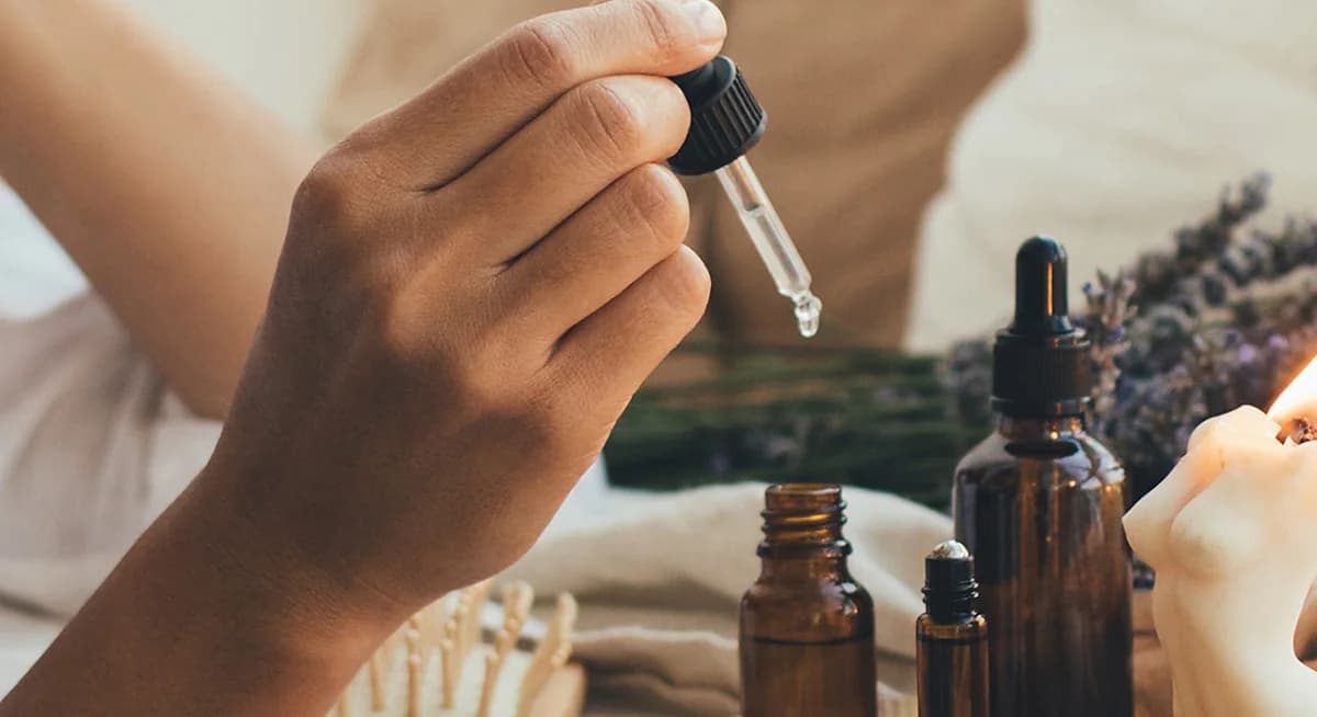 Ätherische Öle mit Pipette neben Lavendel und Kerze