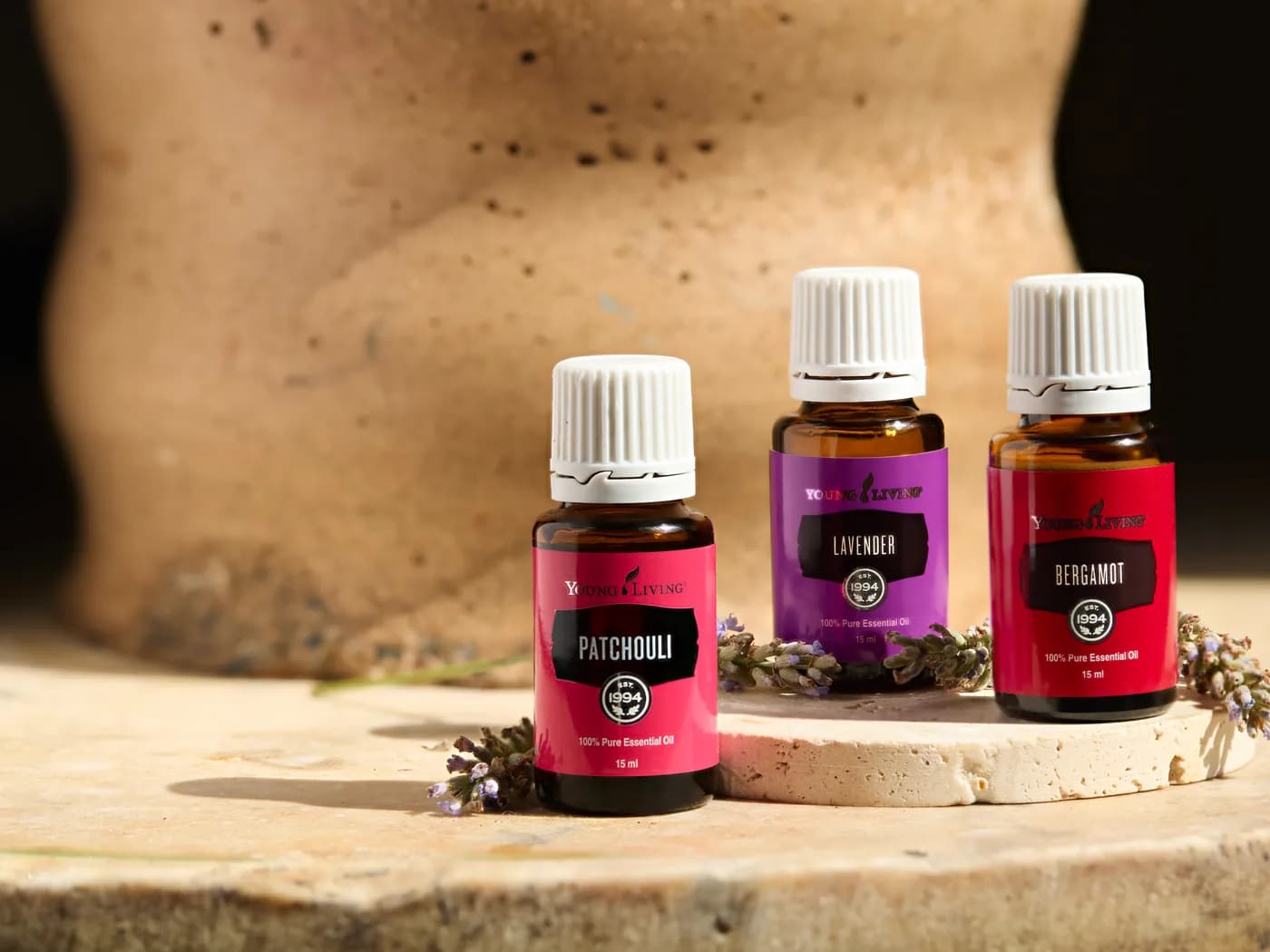 Patchouli, Lavendel und Bergamotte von Young Living auf einer Steinplatte vor einem Tongefäß, mit Lavendelzweigen