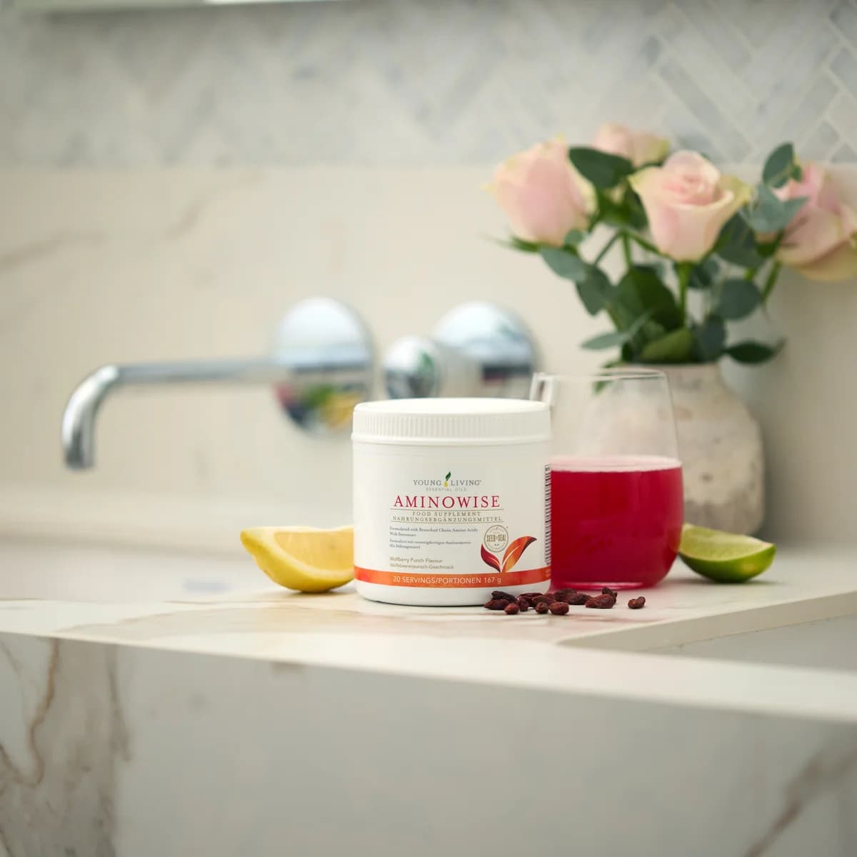 Eine Dose Young Living AminoWise steht auf einer Marmorablage neben einem Glas mit rotem Getränk sowie Zitronen- und Limettenstücken.