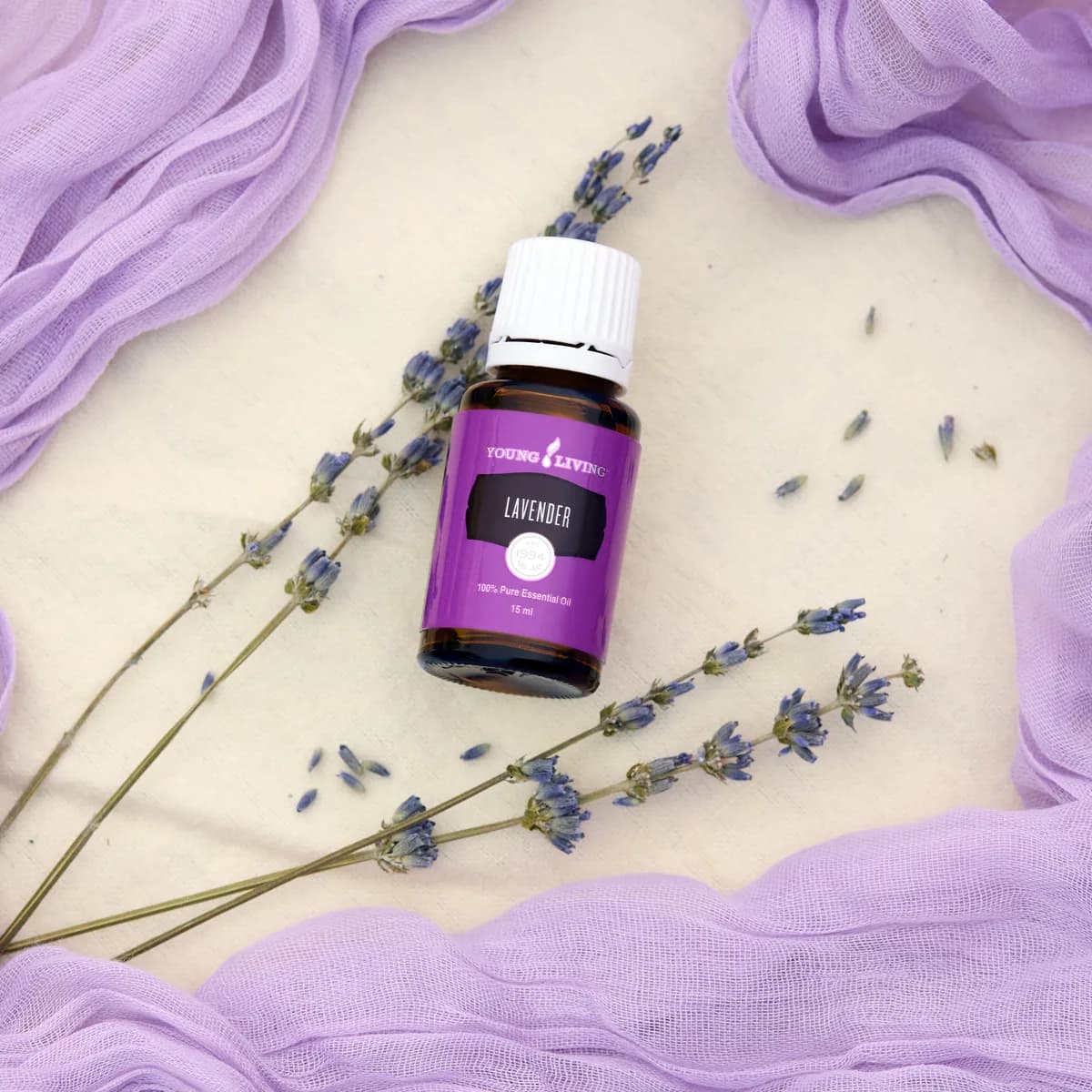 Ein Fläschchen Young Living Lavendel 15 ml liegt zwischen Lavendelzweigen auf hellem Stoff.