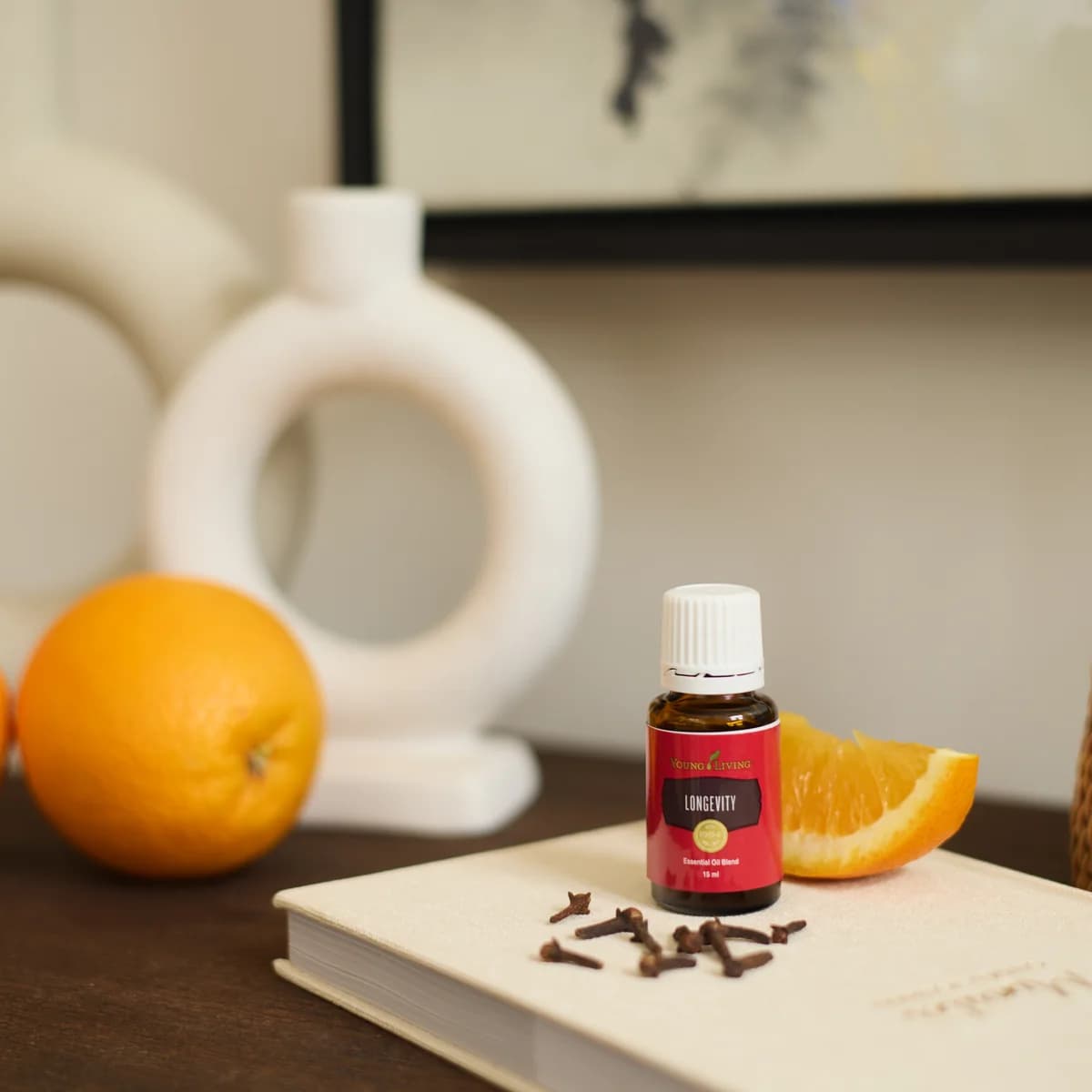 Ein Fläschchen Young Living Longevity 15 ml steht auf einem hellen Notizbuch neben Gewürznelken und einer Orangenspalte.