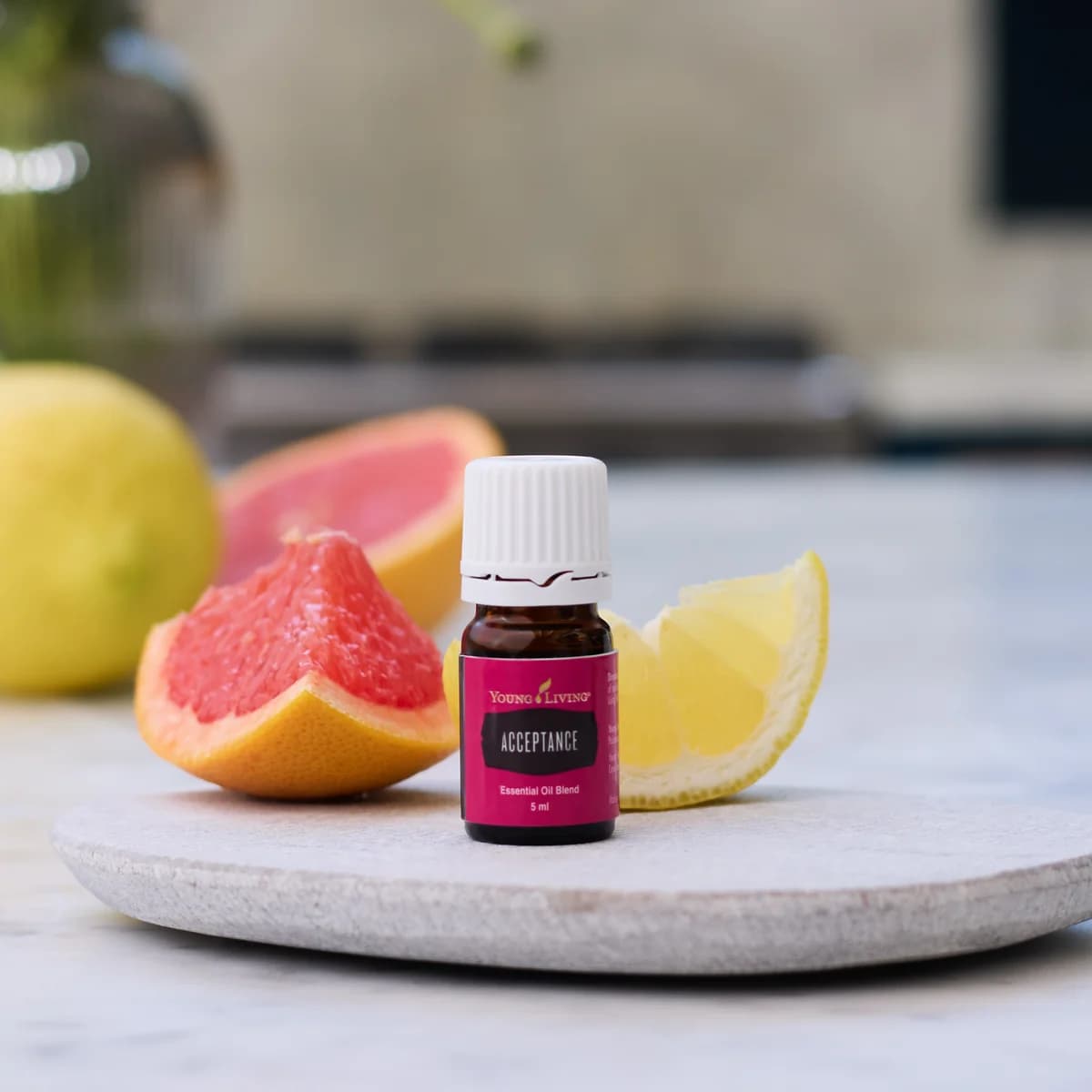 Ein Fläschchen Young Living Acceptance 5 ml steht auf einer hellen Steinplatte zwischen einer Grapefruitspalte und einem Zitronenschnitz in einer Küche.