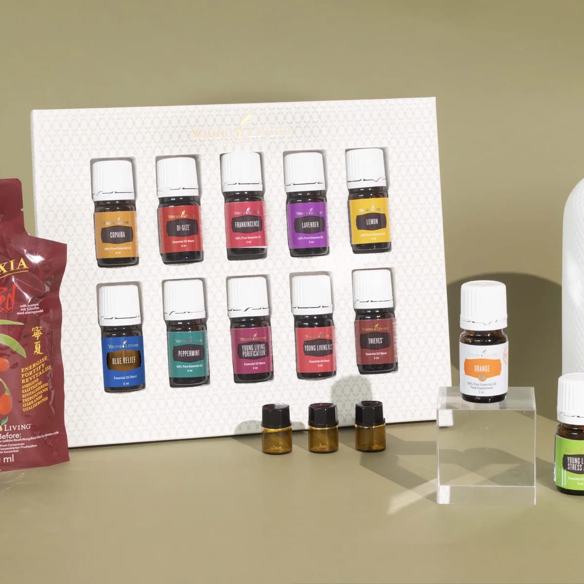 Der weiße Young Living Haven Diffuser steht vor olivgrünem Hintergrund rechts neben einem Starter-Set mit zehn Ölfläschchen, einer Flasche V-6 und NingXia Red.