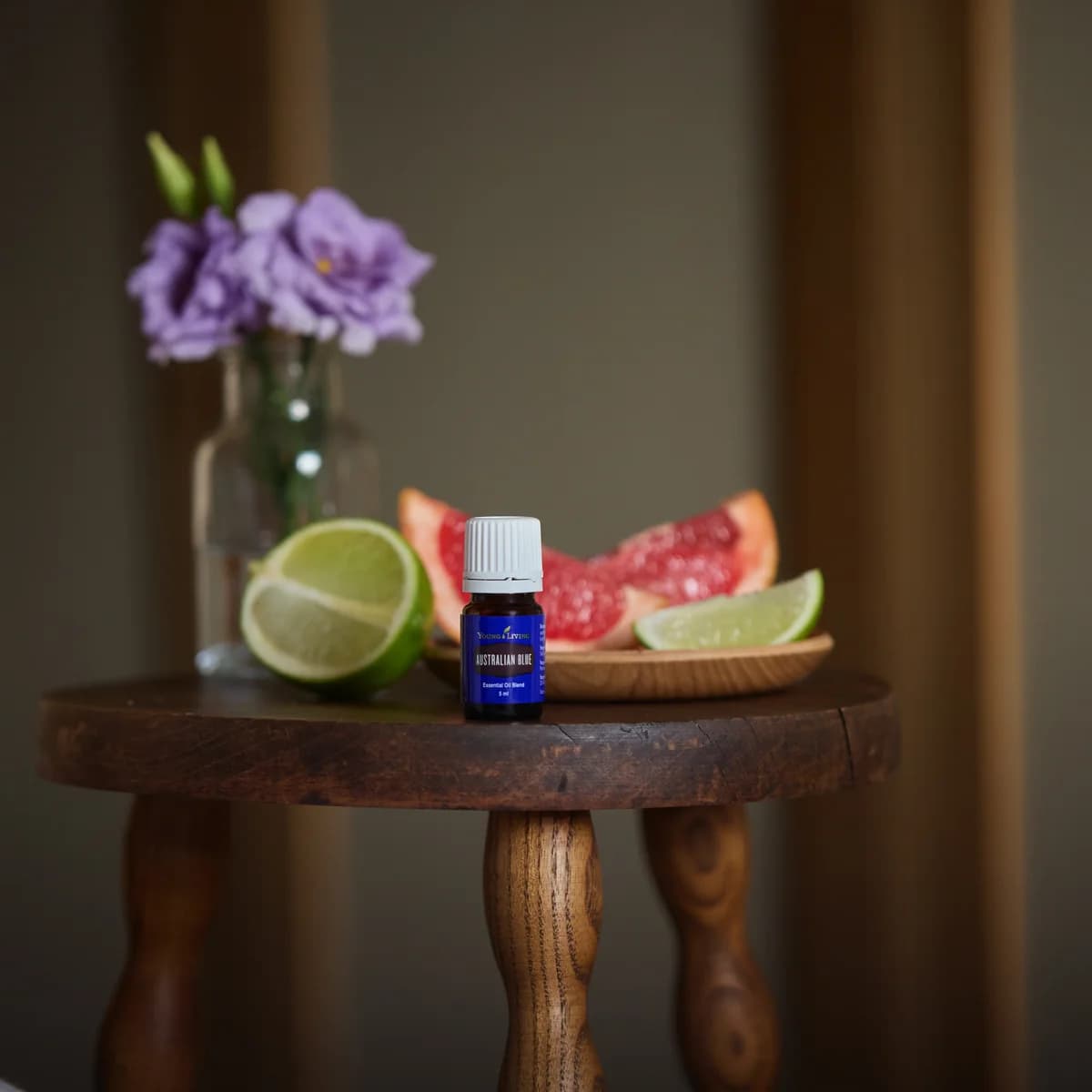 Ein Fläschchen Young Living Australian Blue 5 ml steht auf einem kleinen Holzhocker neben Limette und Grapefruitstücken.