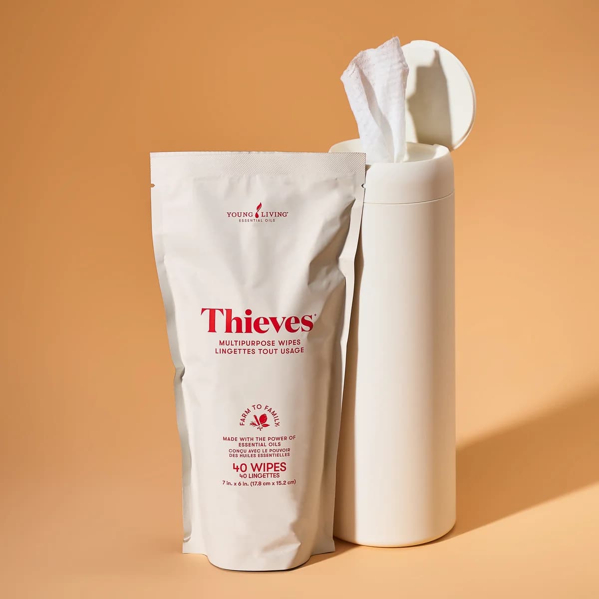 Die Young Living Thieves® Multi-Purpose Wipes Collection vor orangem Hintergrund, ein Nachfüllbeutel neben einem weißen Spender mit herausgezogenem Tuch.