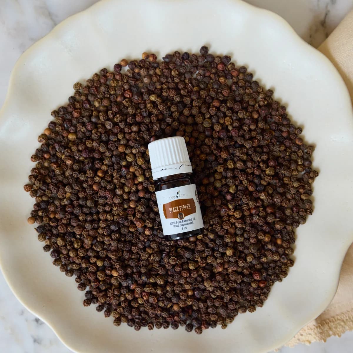 Ein Fläschchen Young Living Black Pepper+ 5 ml liegt auf einer Schicht schwarzer Pfefferkörner.