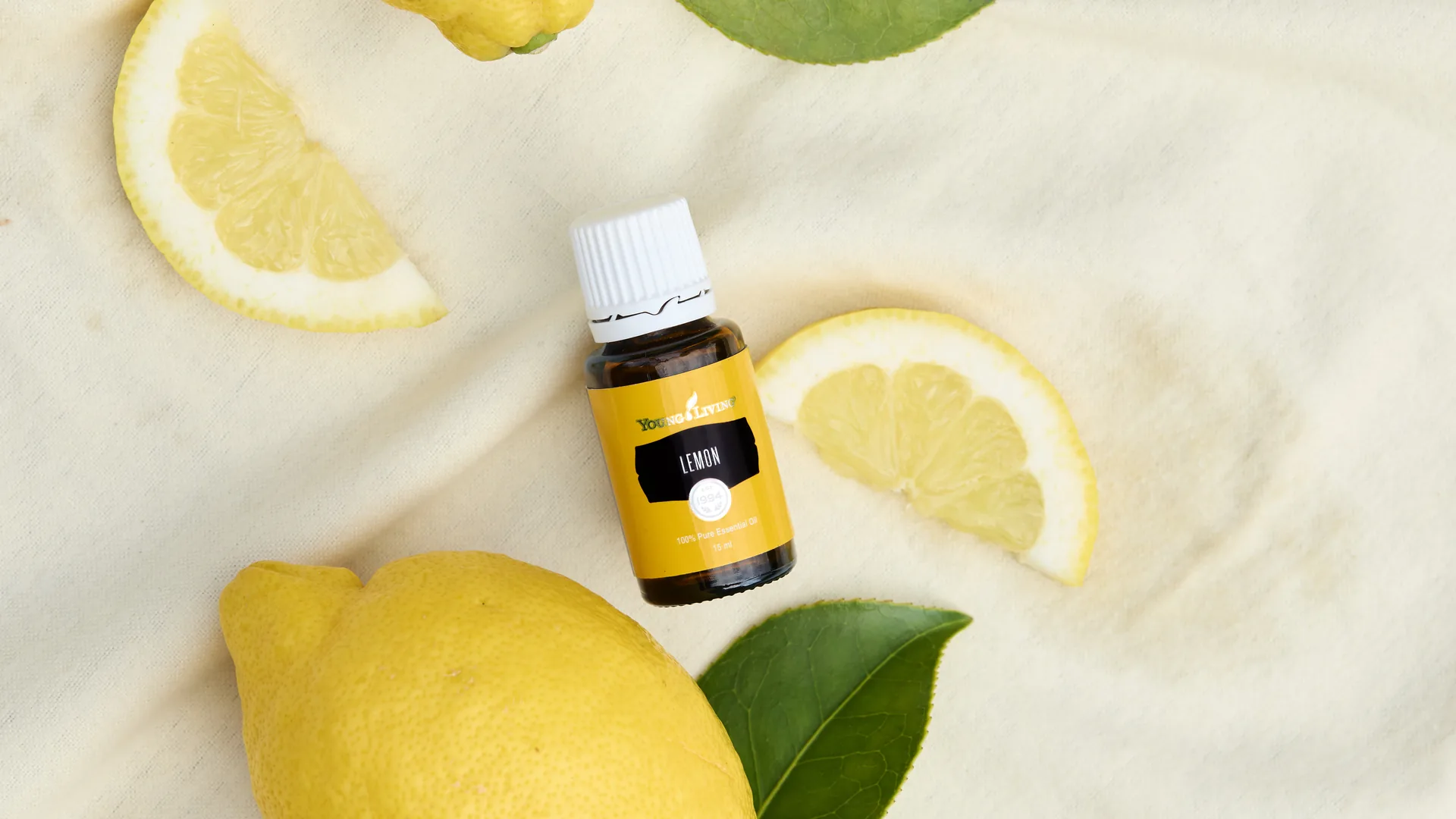 Young Living Zitronenöl mit frischen Zitronen, Zitronenscheiben und Blättern auf einem hellen Tuch